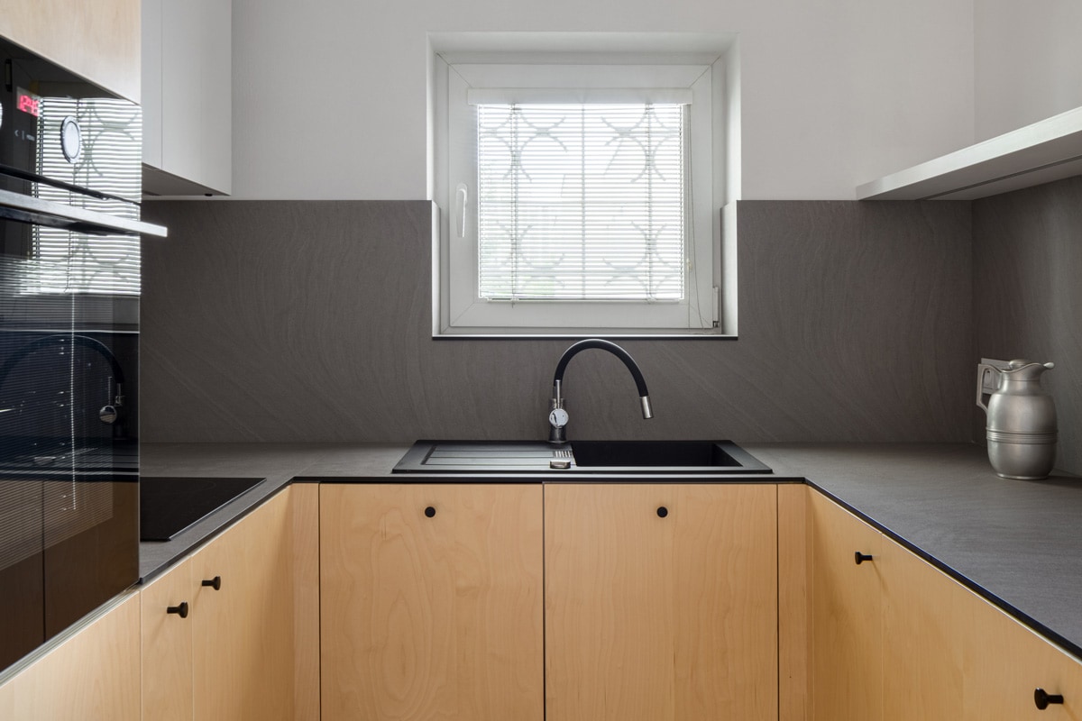 Modern kitchen with birch plywood on cupboards, dark veneer countertops, black sink and tap and small, square window