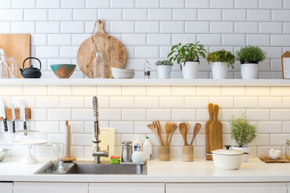 Modern new light kitchen interior. White furniture and white tile pattern wall. Utensils, decoration and pots with fresh herbs in domestic kitchen.