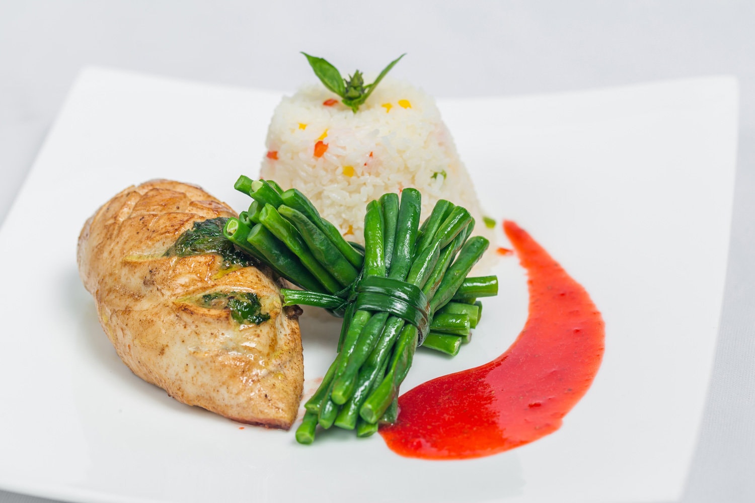 Pan roasted chicken breast with long green beans and light vegetable rice platter. Food decorating with red sauce on a white plate. Isolated white background.
