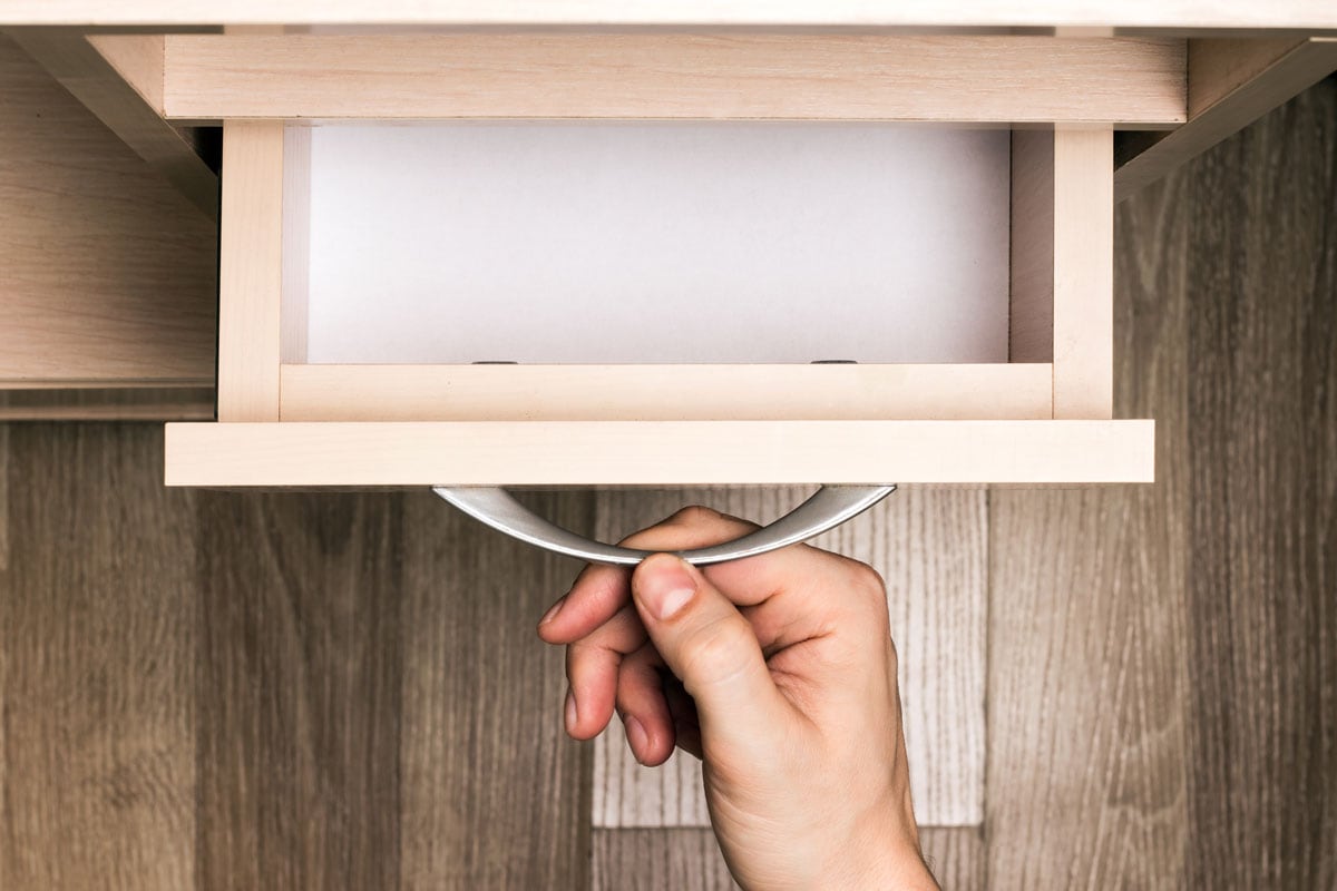 Person's hand pulls out a pull-out empty furniture drawer
