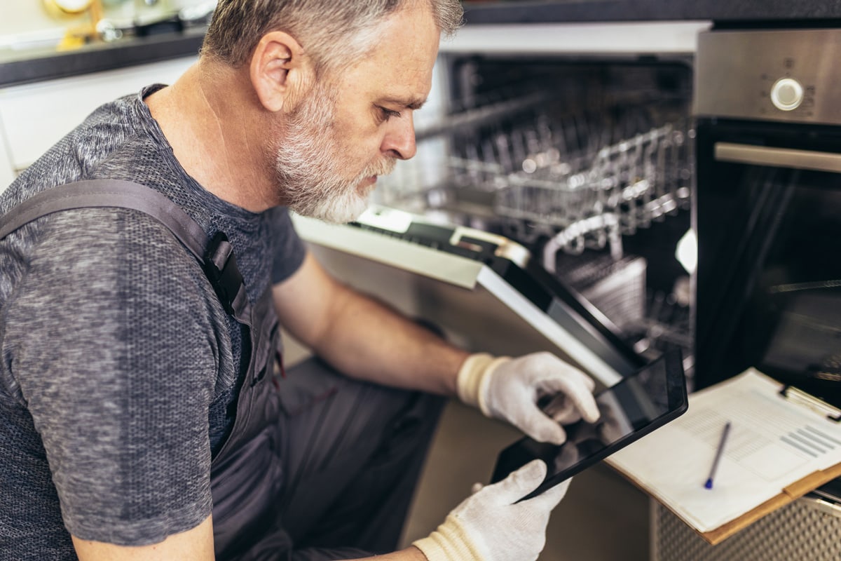 Portrait Of Male Technician Repairing Dishwasher In Kitchen