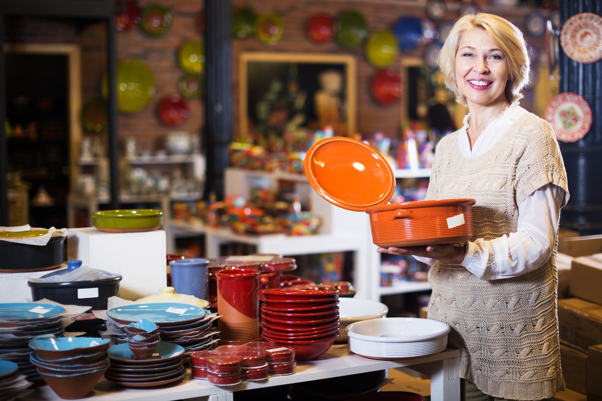 Positive mature woman selecting ceramic tableware in shop cookware.