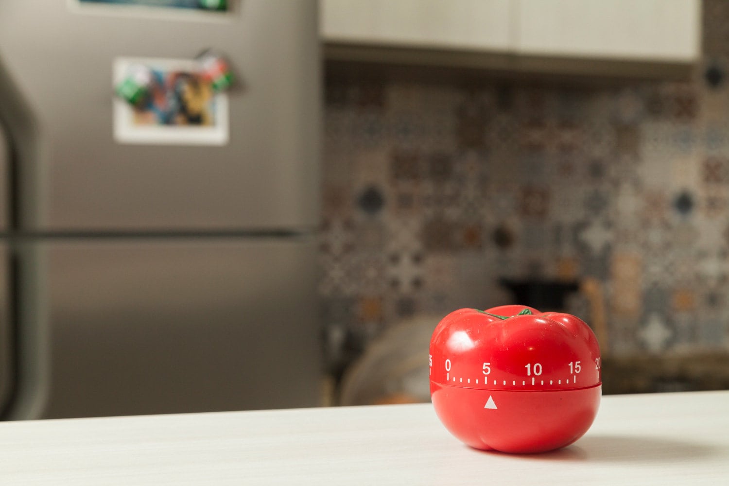 Red tomato-shaped kitchen timer with cooking in the background. To let you know when to turn off the stove and food is ready. Brazilian cuisine. Kitchen concept. Household appliance concept.