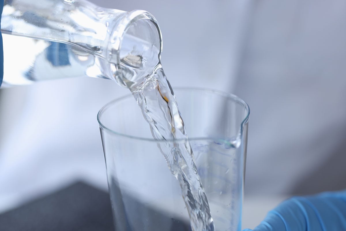 Scientist chemist pouring water from transparent bottle into flask in laboratory