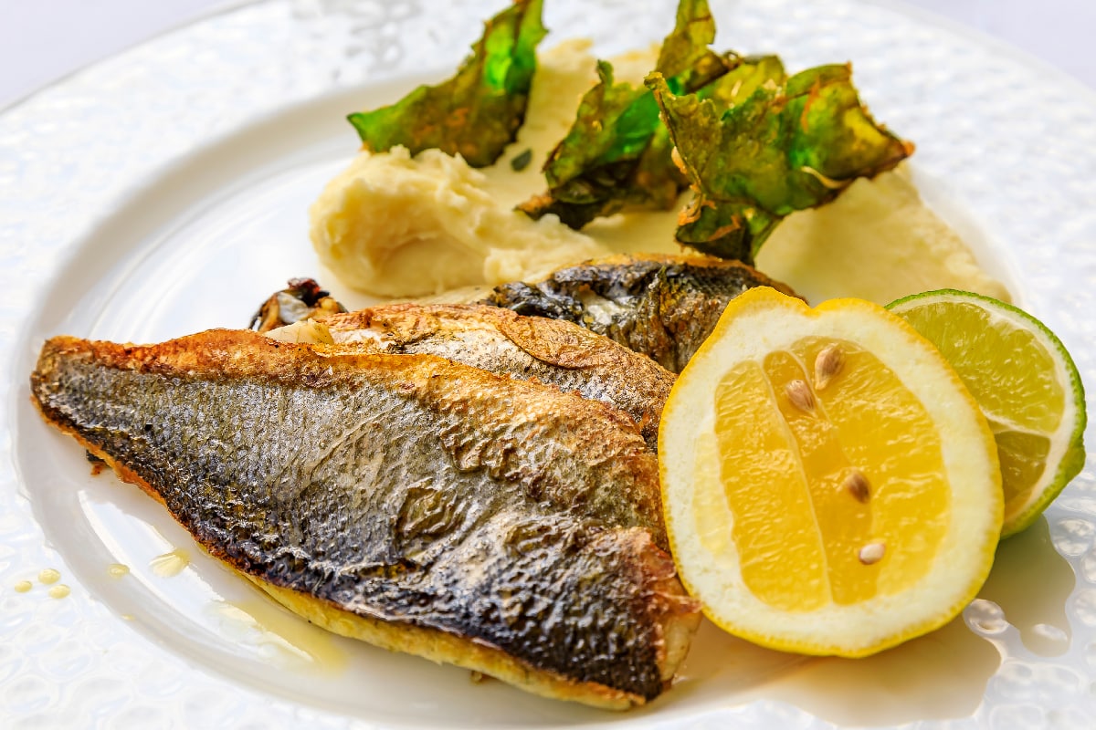 Sea bass served with lemon and lime wedges, and mashed potatoes with fried kale chips