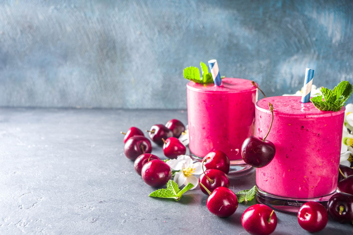 Sweet cherry smoothie drink in glass jars with mint leaves and fresh berries