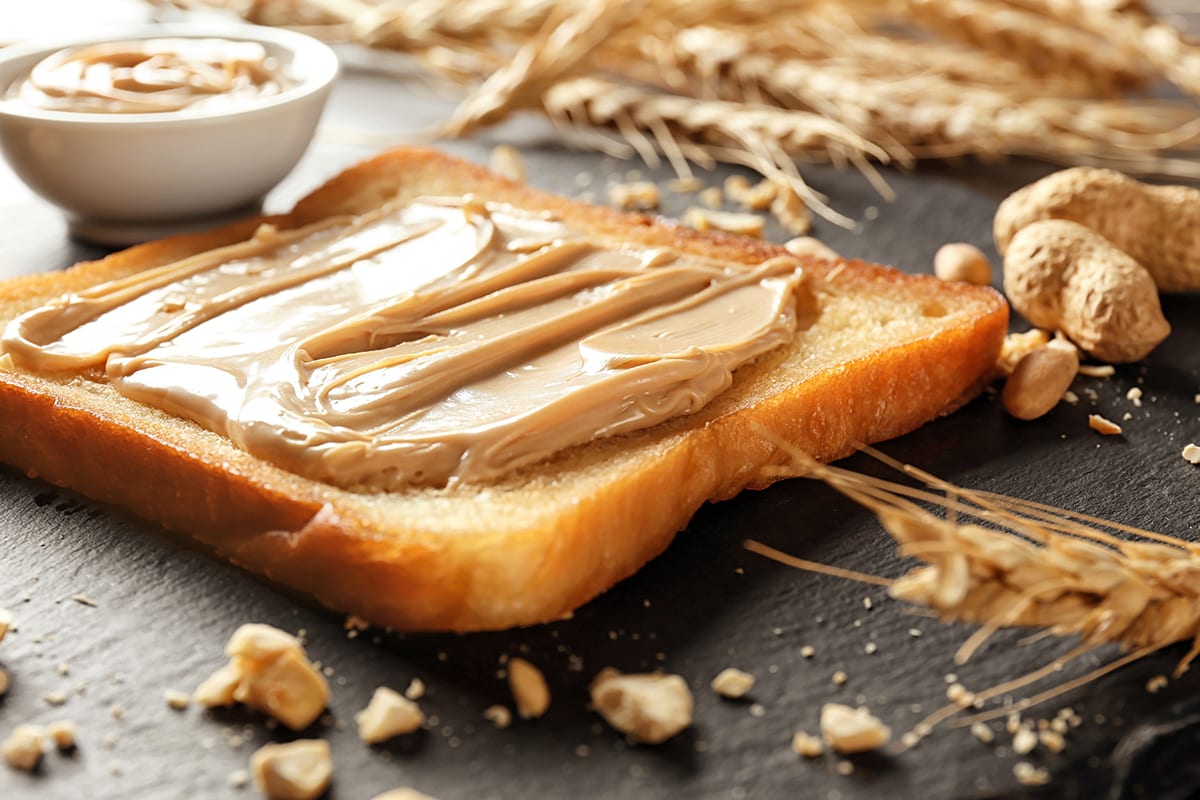 Tasty toast with peanut butter on slate plate