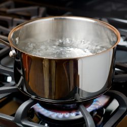 Water bubbles and boils on a gas stove or range in a home kitchen. Blue flame and stainless steel pot - How Long Do All Clad Pans Last