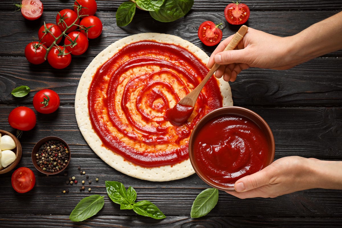 woman-spreading-tomato-sauce-onto-pizza