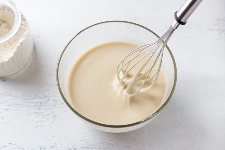 A glass bowl of dough for Finnish pancakes with a whisk and a jar of flour on a light gray background, top view. Can You Make Crepes Without a Blender?