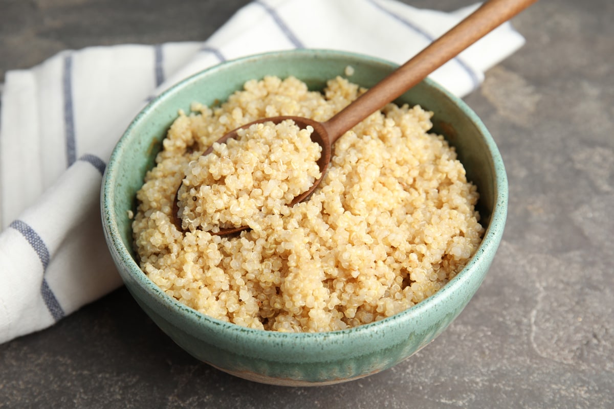 Composition with cooked quinoa in bowl and wooden spoon on table, Do You Cook Quinoa Before Adding It To Soup?