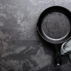 Empty cast iron frying pan on dark grey culinary background, view from above - How To Strip Cast Iron Without Oven Cleaner