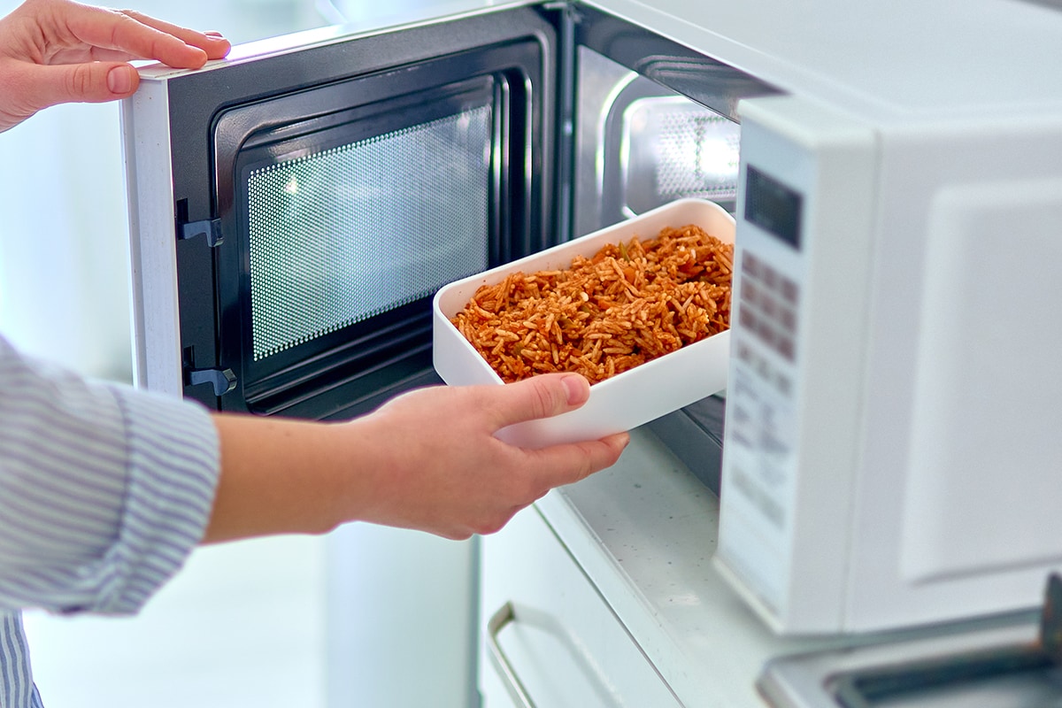 Hands warming up a container of food in the modern microwave oven