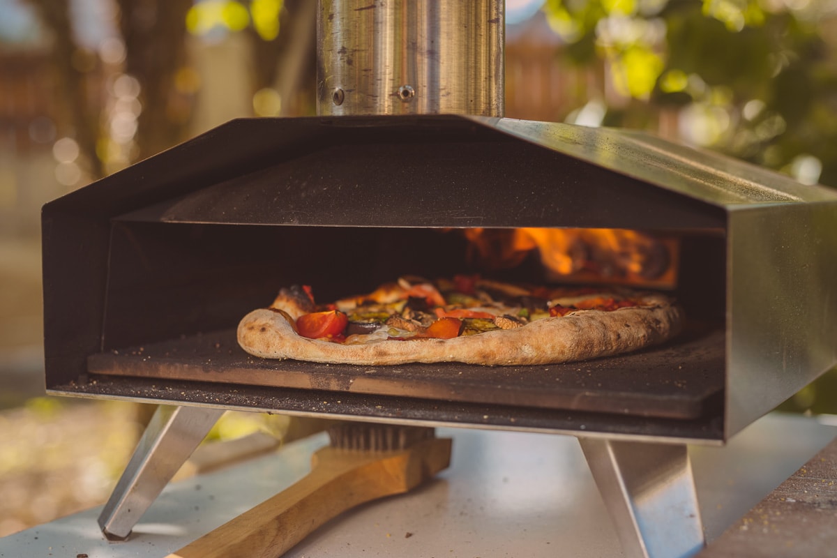 Home made pizza is inserted in a portable aluminium home oven for pizzas.