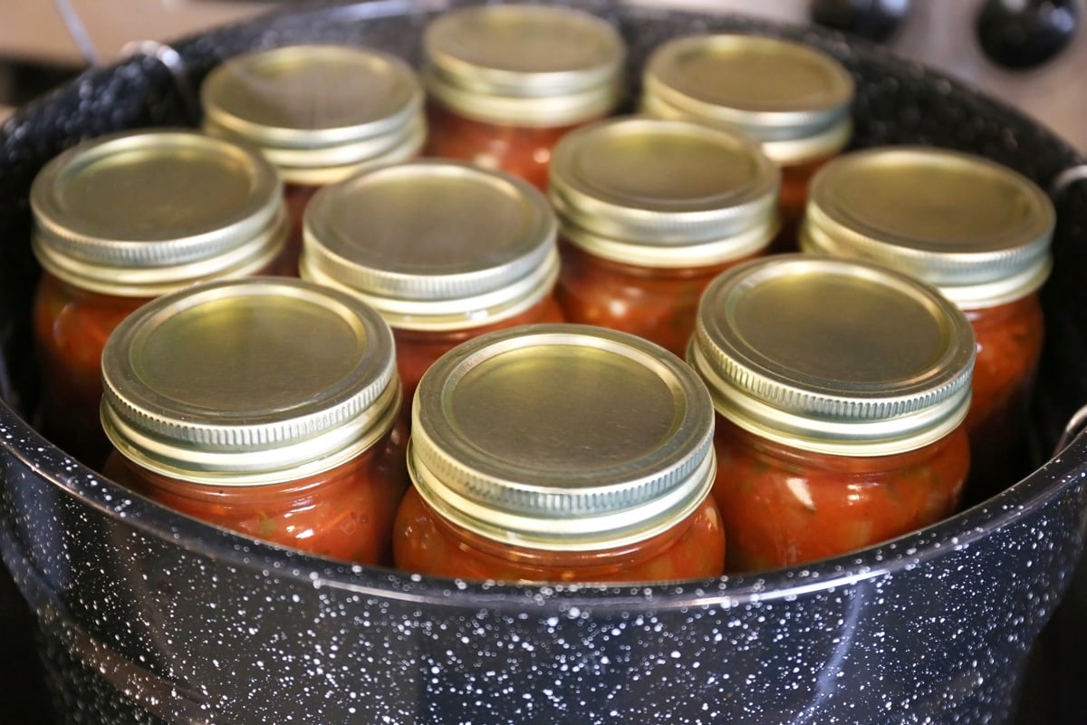 Jars of freshly canned homemade salsa are cooling after boiling in a large kitchen pot.