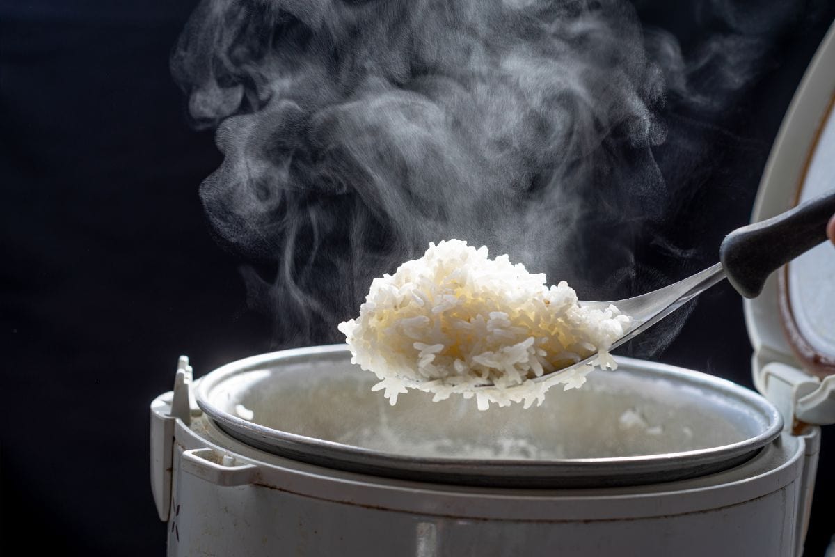 Jasmine rice cooking in electric rice cooker with steam on dark background. Soft Focus,