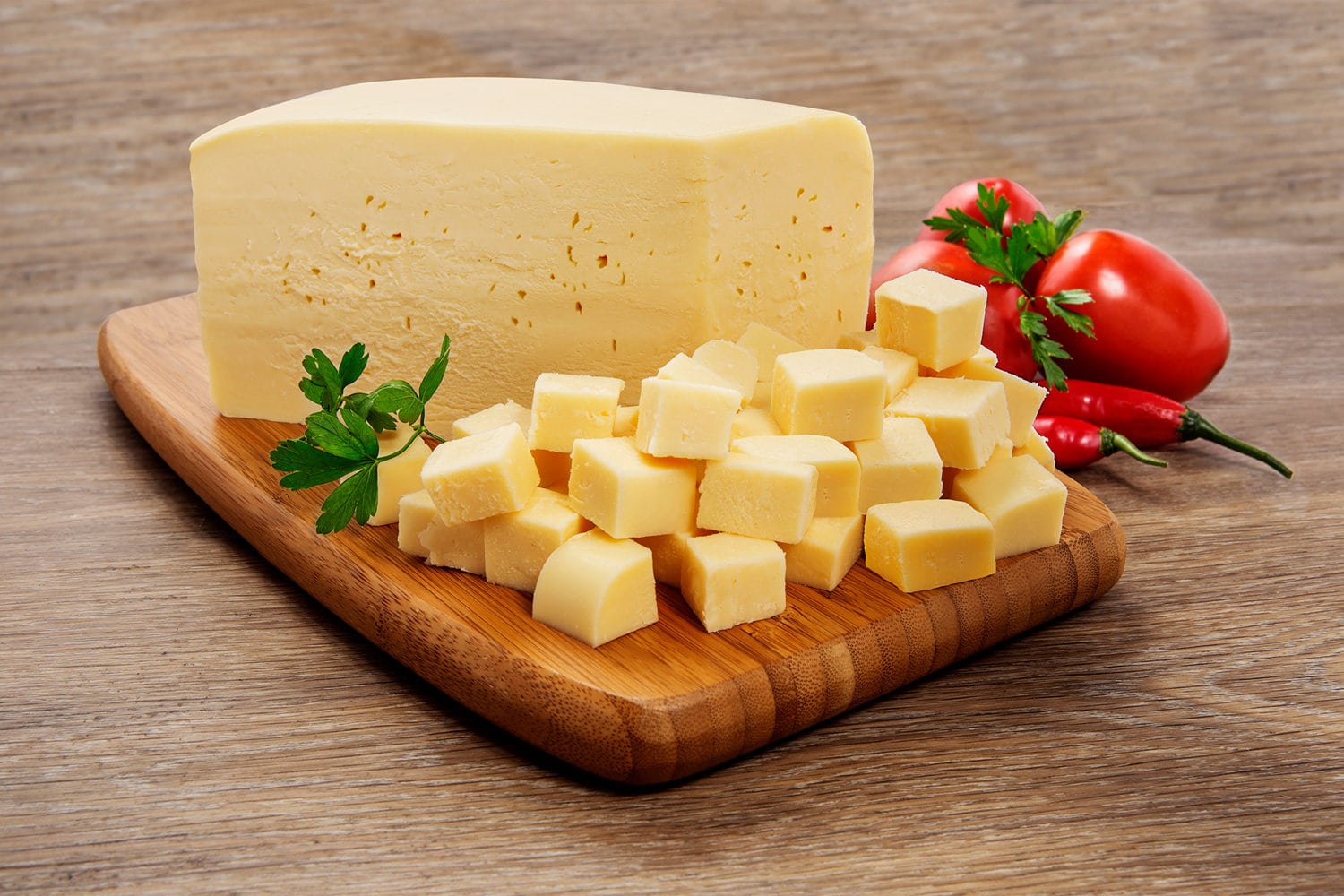 Mozzarella cheese in pieces and cut into cubes on wooden cutting board on wooden background. 