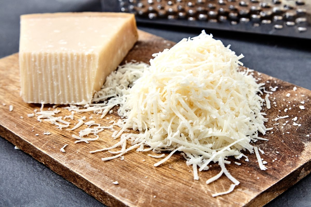 Piece and grated parmigiano reggiano or parmesan cheese on wwood board on checkered napkin . Grated parmesan uses in pasta dishes, soups, risottos and grated over salads. - Can You Use Mozzarella Instead Of Parmesan In Alfredo