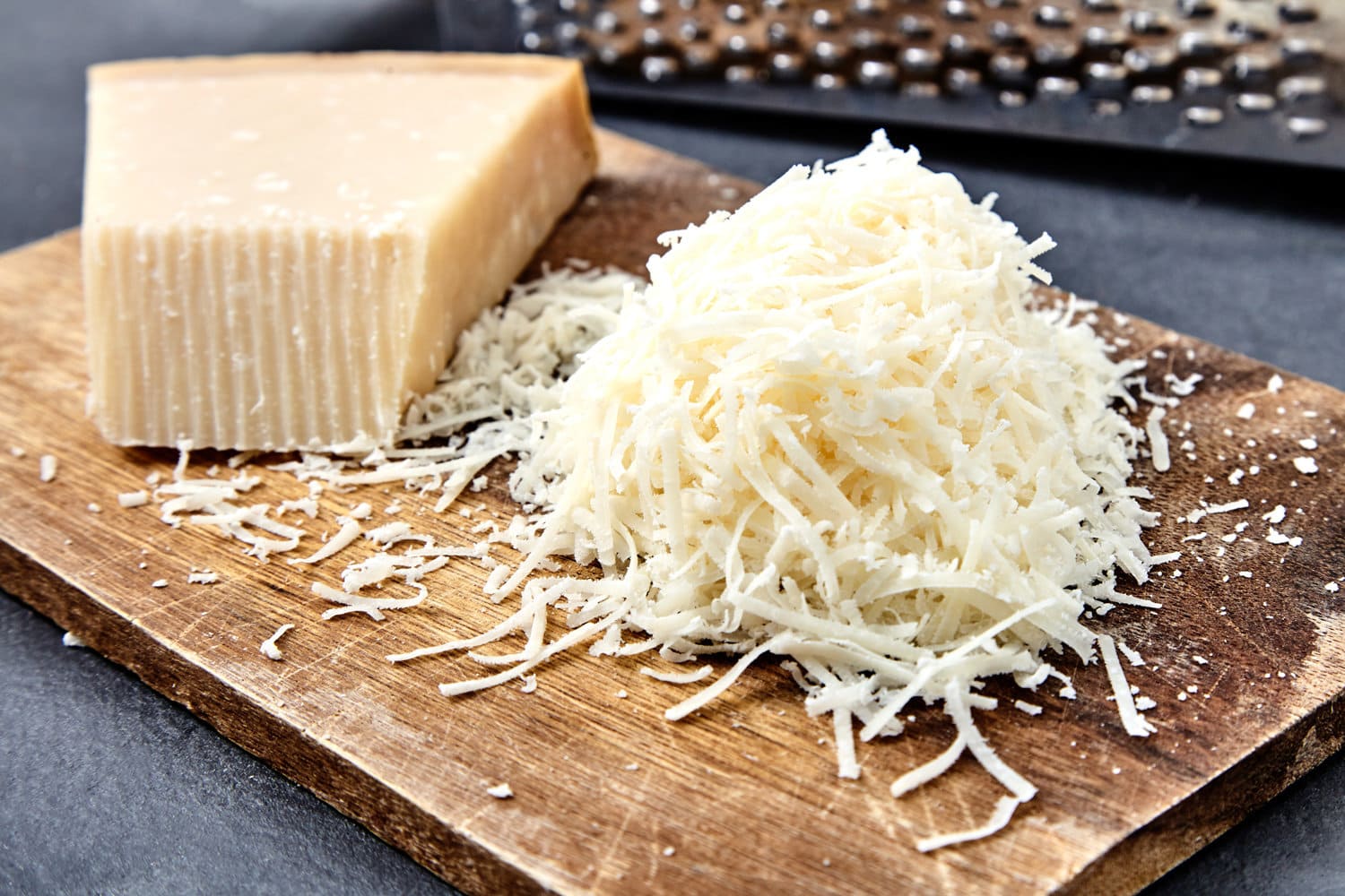 Piece and grated parmigiano reggiano or parmesan cheese on wwood board on checkered napkin . Grated parmesan uses in pasta dishes, soups, risottos and grated over salads. 