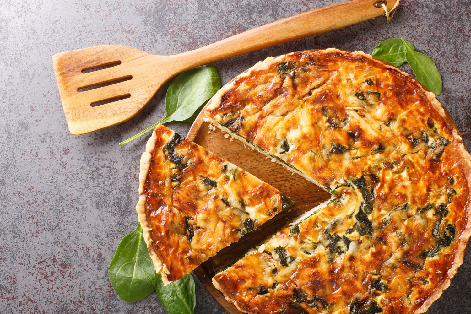 Quiche Florentine is a fresh spinach quiche baked in a homemade pie crust to serve for brunch or breakfast for dinner on gray table close-up. Hotizontal top view from above 