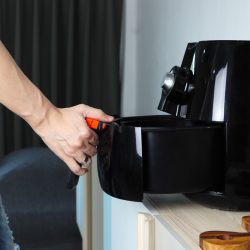 Right hand of man holding the tray of the black deep air fryer or oil free fryer appliance which is on the wooden table in the white kitchen ( air fryer ) during lunch with family members, Do You Need To Flip Burgers In An Air Fryer?