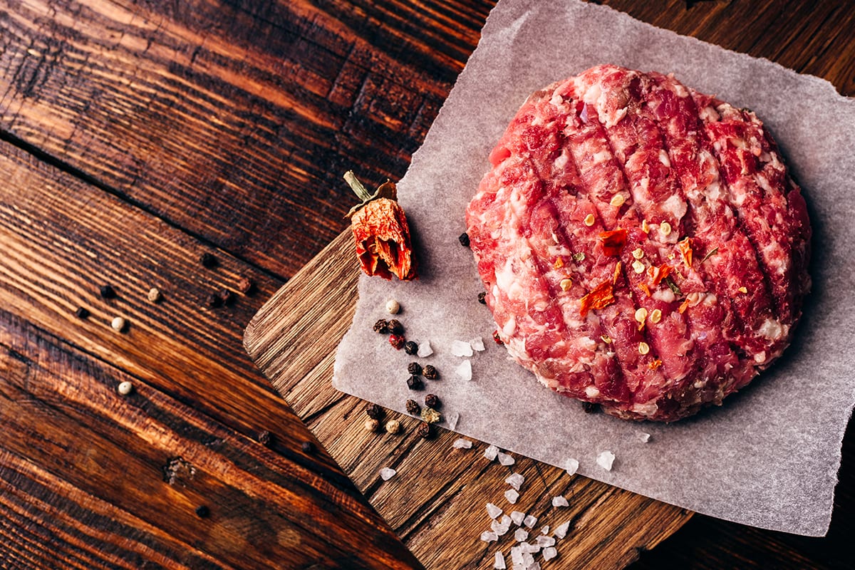 Raw round patty with spices on wax paper for burger