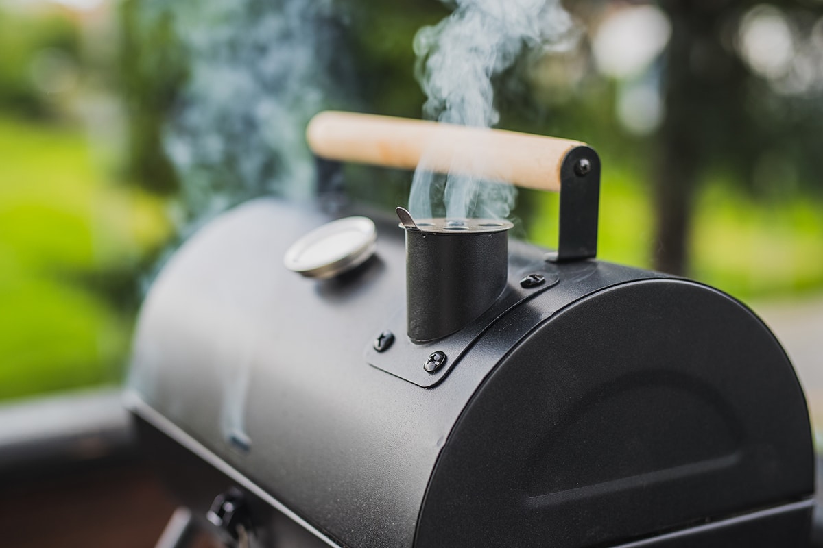 Smoke coming out of a smokestack of a small black smoker grill