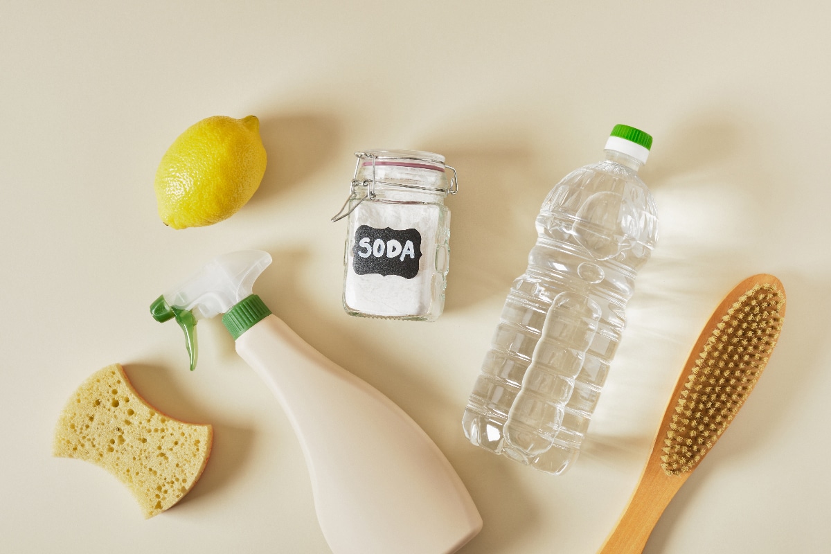 Soda can, spray bottle, vinegar, lemon, wooden brush and sponge on beige table