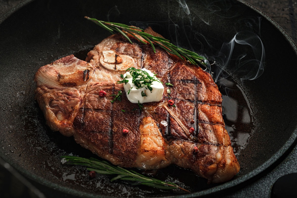 T-bone steak steaming in a grill pan with spices, rosemary and butter
