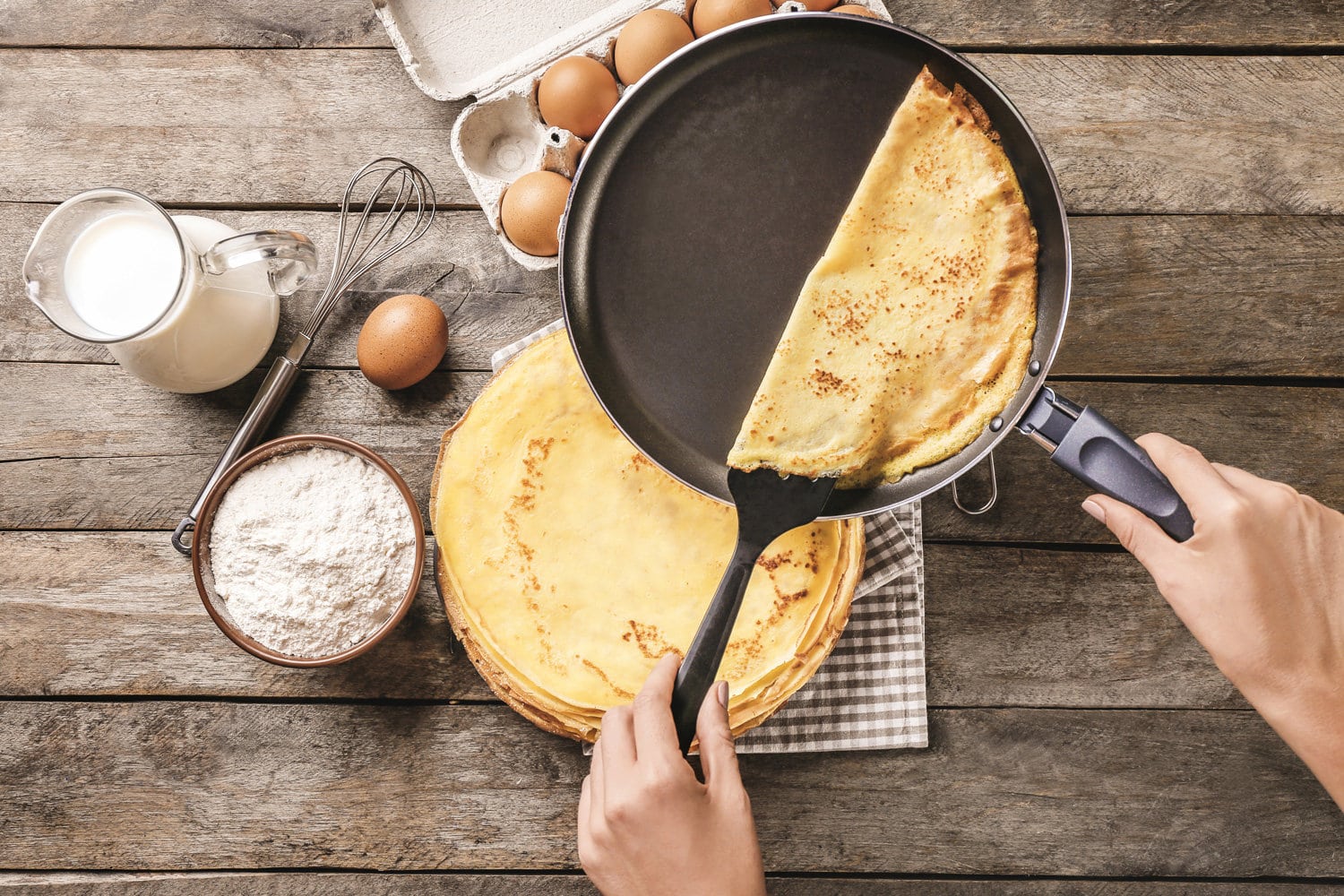 Woman making thin pancakes on frying pan in kitchen.