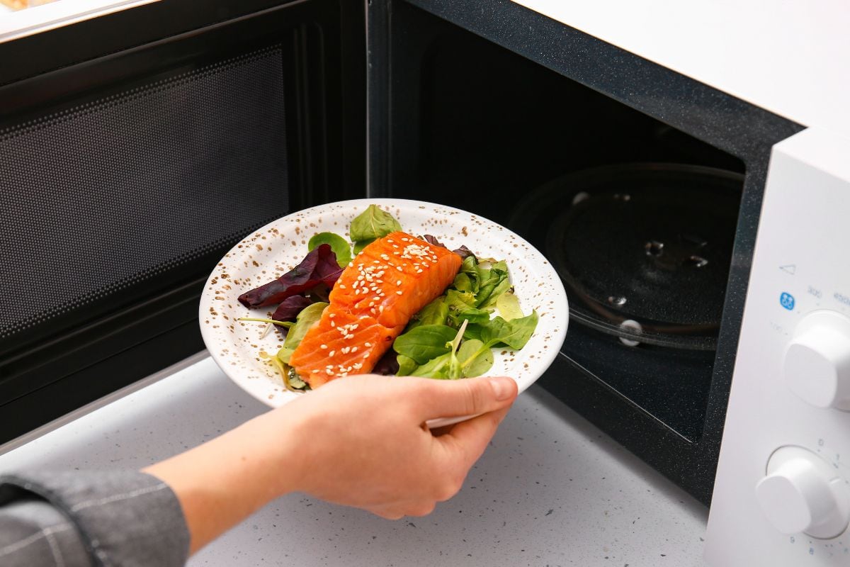 Woman putting plate with food in microwave oven