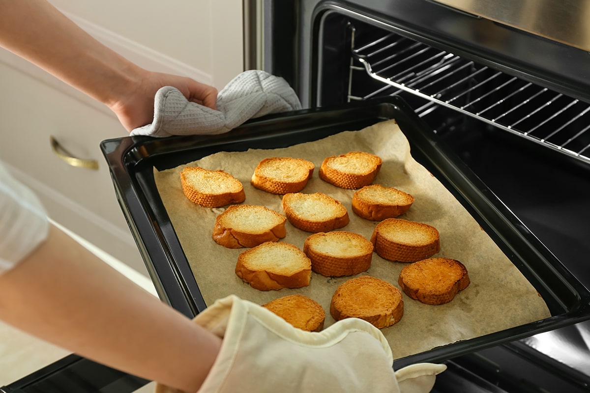Woman taking baking sheet with toasted bread out of oven