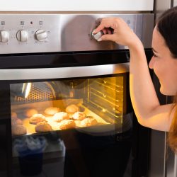 Young Woman Using Microwave Oven For Baking Fresh Cookies In Kitchen, Should Ovens Get Hot On The Outside?