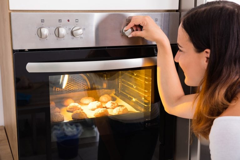 Young Woman Using Microwave Oven For Baking Fresh Cookies In Kitchen, Should Ovens Get Hot On The Outside?