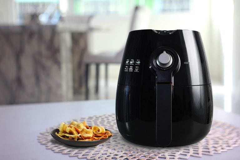 a black air fryer or oil free fryer appliance is on grey table in the dining room with deep fried banana chips in small black dish, Do Air Fryers Get Hot On The Outside?
