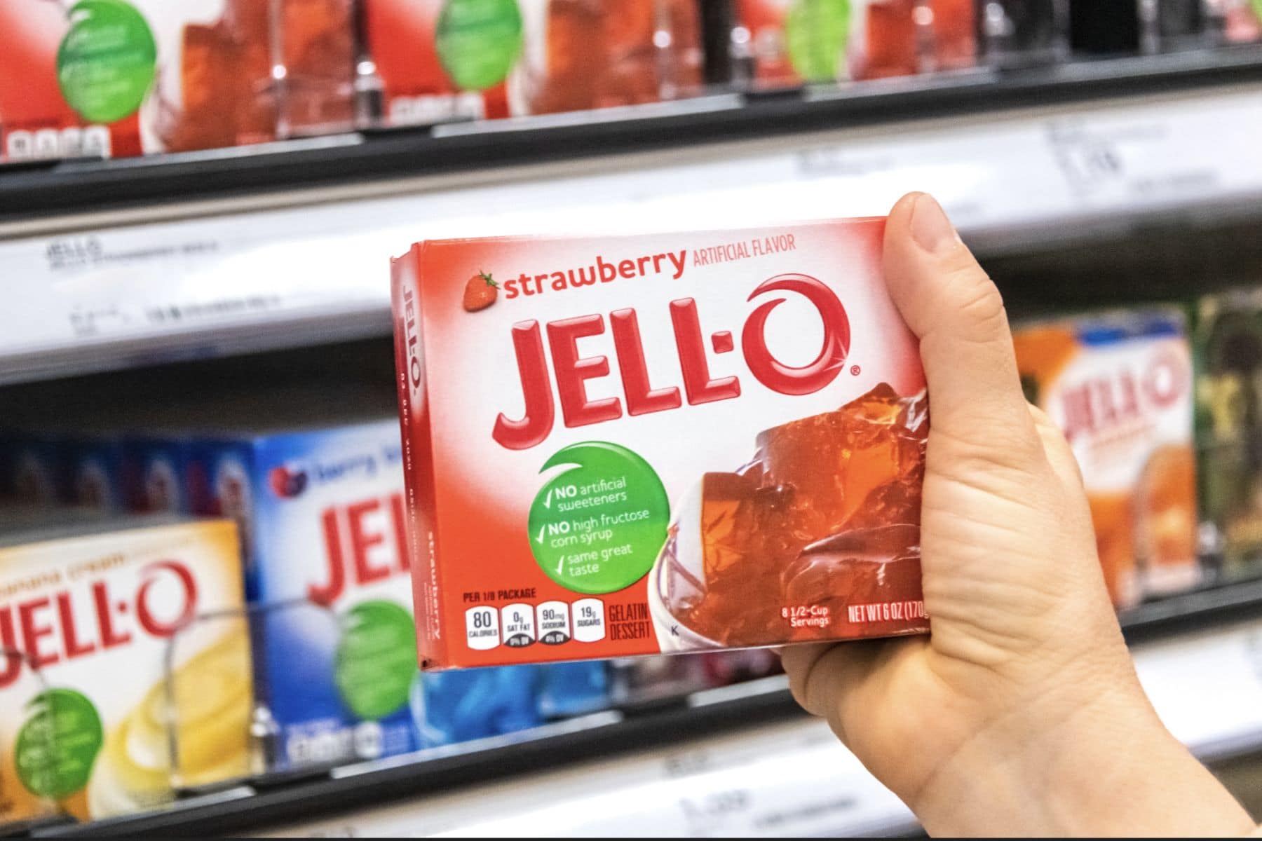 shoppers hand holding a box of Jell-o strawberry gelatin dessert at a supermarket aisle