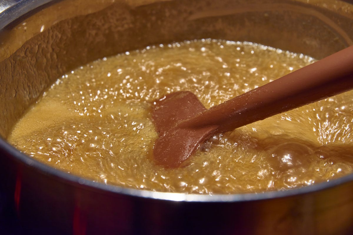 A ladle in a pot with a boiling mix of sugar, suryp, butter and cream in making of butterscotch