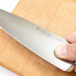 A man hand holding a cooking knife with a wooden chop board, Does Wusthof Replace Knife Handles?