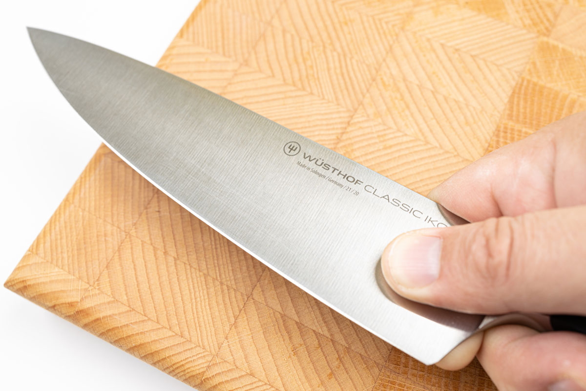 A man hand holding a cooking knife with a wooden chop board