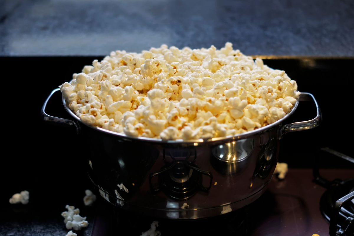 A stainless pan full of popcorn. Focus on the edge of the pan. Soft focus background