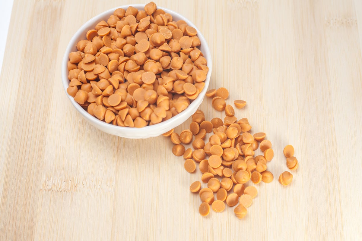 Butterscotch chips in white bowl and scattered over a wooden table