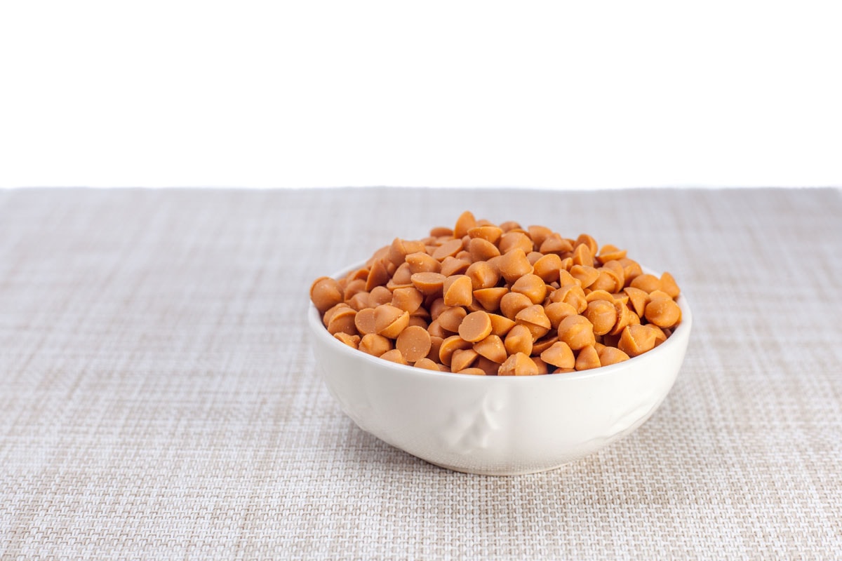Butterscotch chips in white bowl on brown cloth
