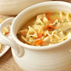 Chicken noodle soup in cream colored ceramic bowl with handles. Plate of crackers and soup tureen in background. Closeup with shallow dof., 11 Soups for Winter that Will Warm Your Heart