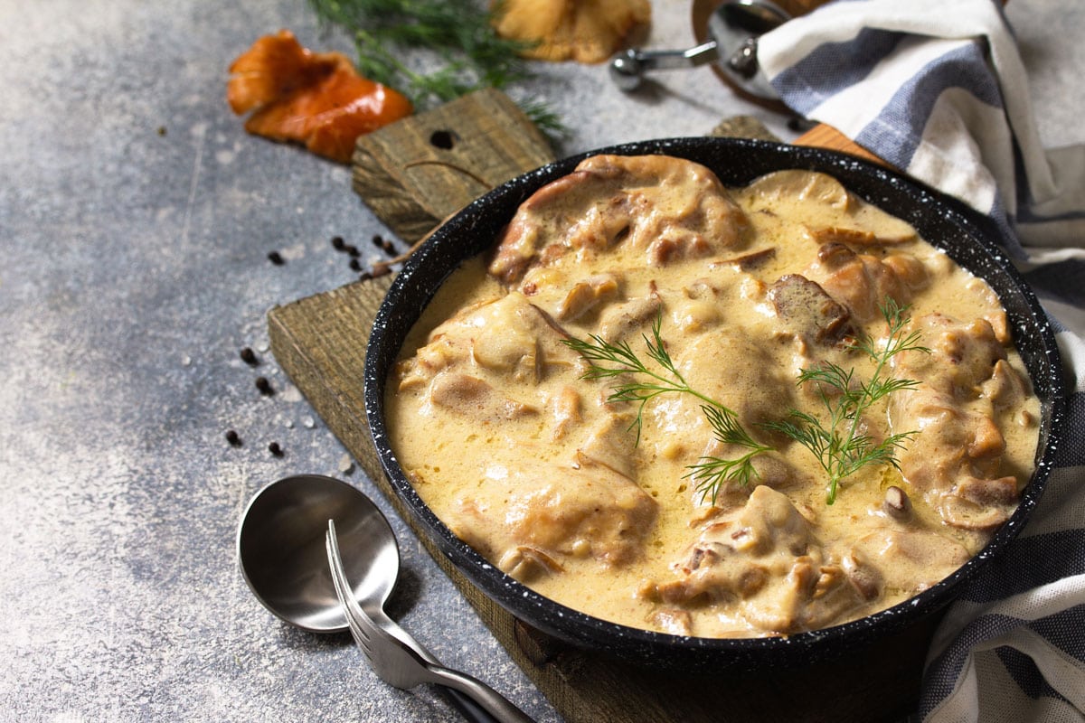 Chicken stewed in a creamy sauce with mushrooms in a pan on a light stone
