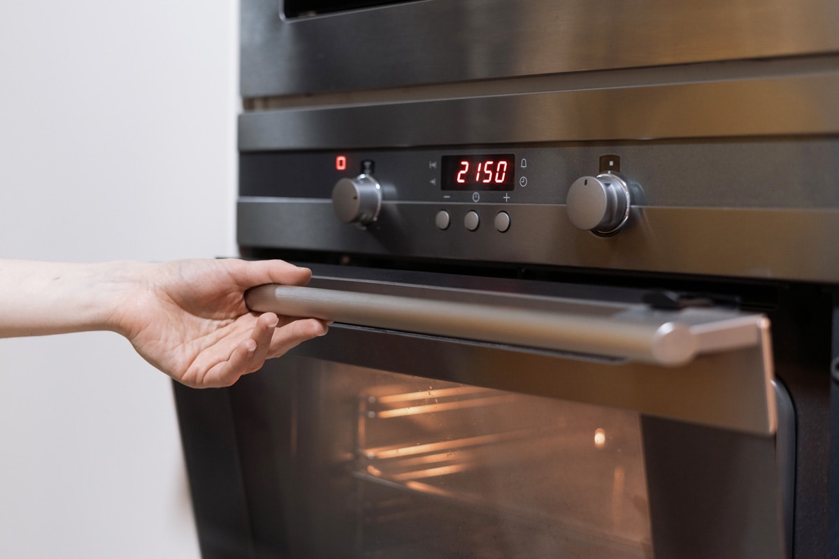 Cropped view of person's hand opening black oven with timer in kitchen.