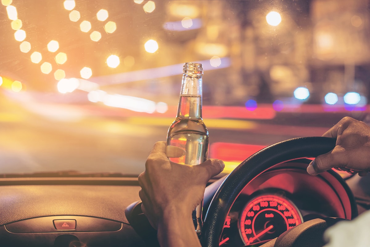 Drunk young man drives a car with a bottle of alcohol