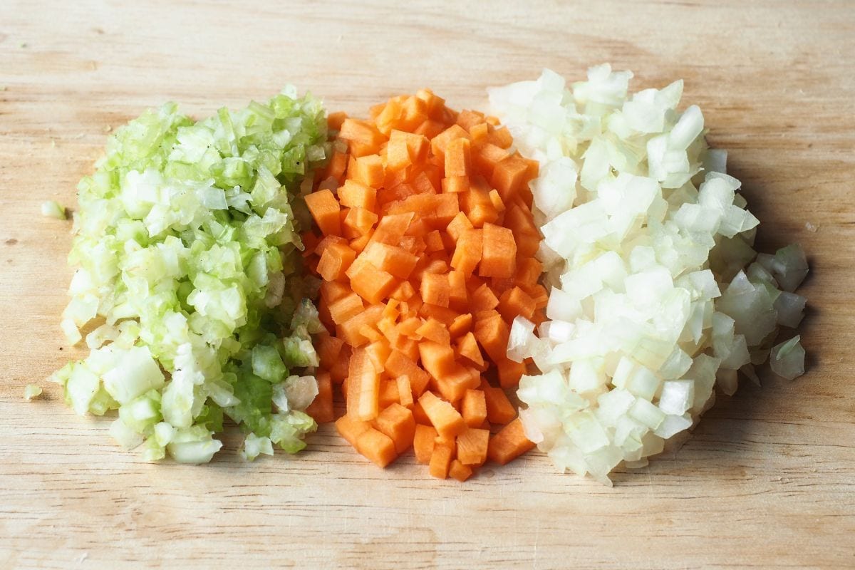 Finely chopped celery, carrot and onion on wooden cutting board.