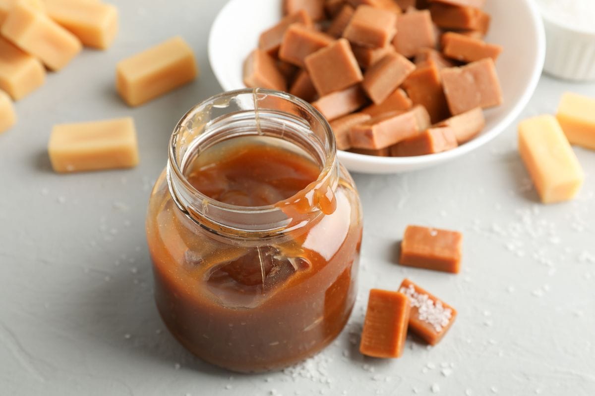Glass jar with salted caramel and candies on grey background, close up.