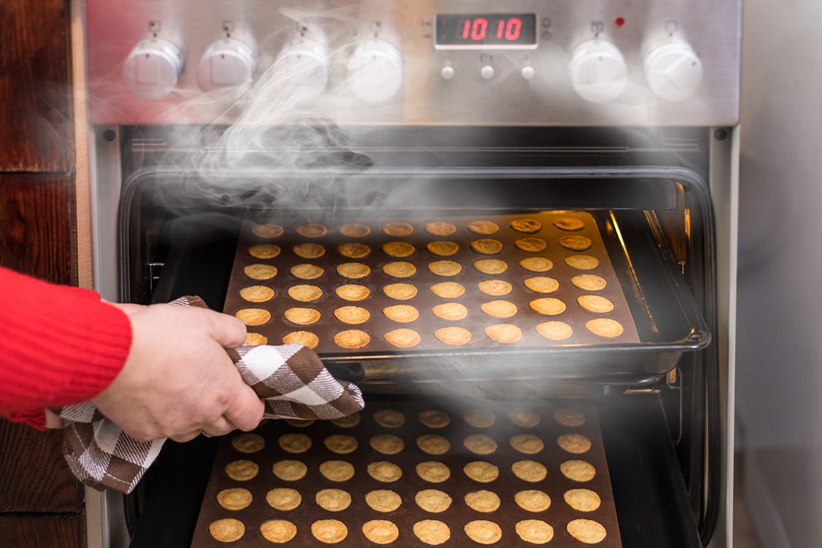 Hand taking hot nutty cookies out of a steaming convection oven of kitchen oven