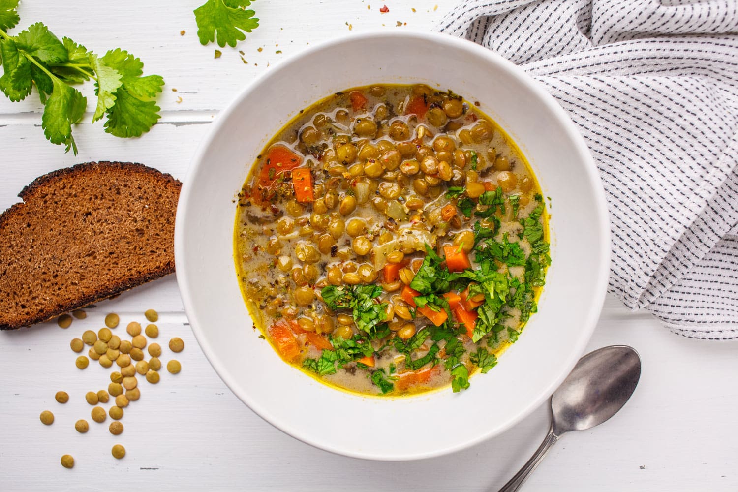 Homemade vegan lentil soup with vegetables and cilantro, white wooden background, top view. Indian vegetarian cuisine. 
